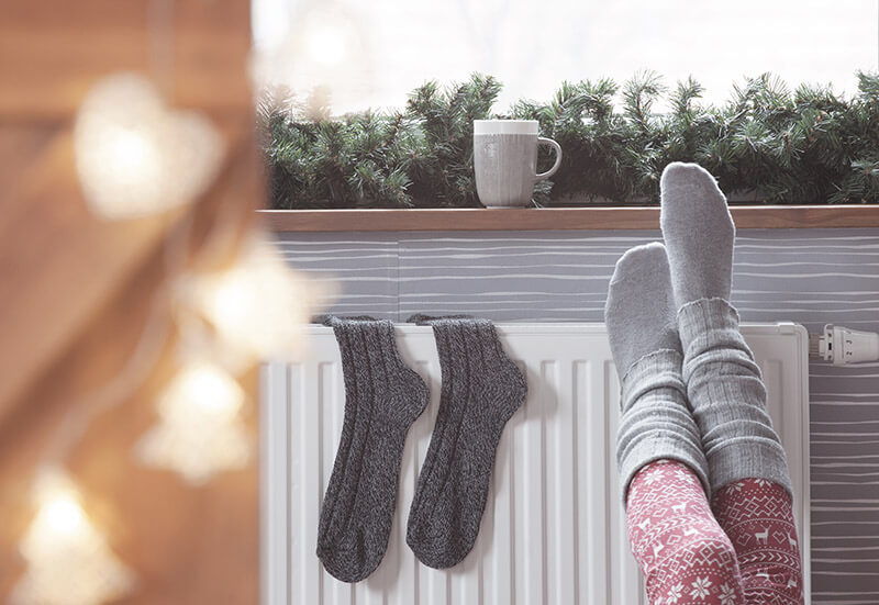 Cozy socks on heater with holiday decor around