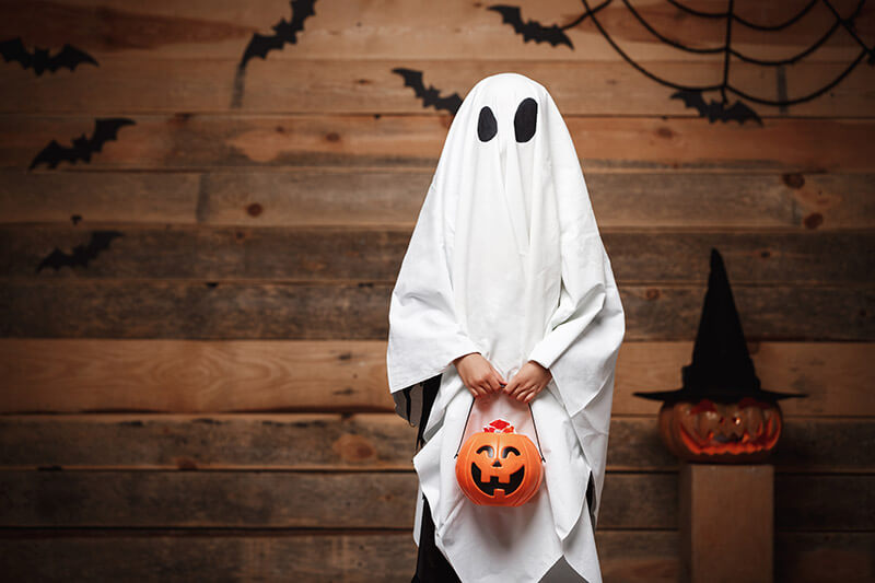 Kid dressed as ghost holding a jack-o-lantern
